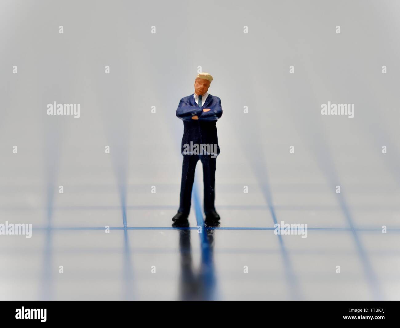Statuetta in miniatura imprenditore con le braccia incrociate in piedi su un quadrato blu superficie lucida. Foto Stock