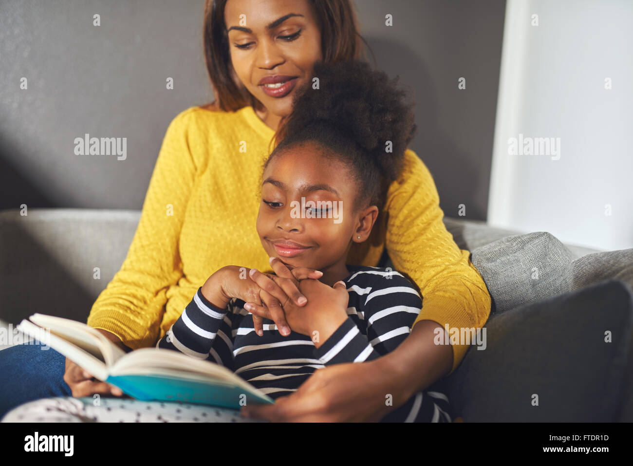 Nero a mamma e figlia la lettura di un libro seduti sul divano a sorridere Foto Stock