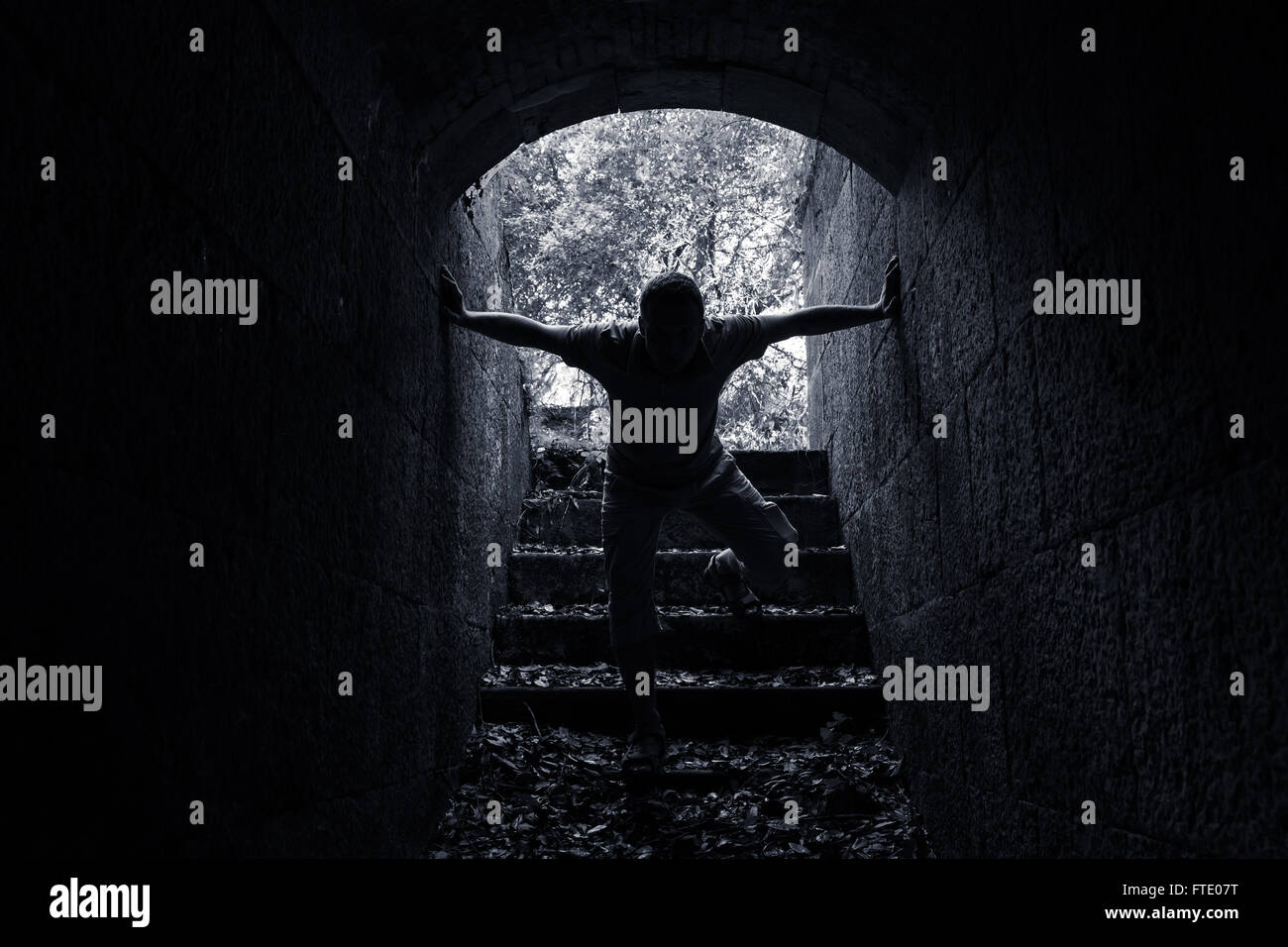 Giovane uomo entra nel buio del tunnel di pietra in bianco e nero lo foto chiave Foto Stock