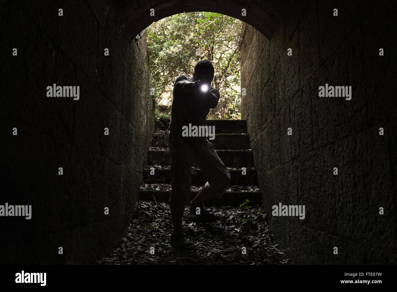 Spaventata giovane con una torcia elettrica entra nel tunnel di pietra e guarda al buio, la correzione delle tonalità foto effetto filtro Foto Stock