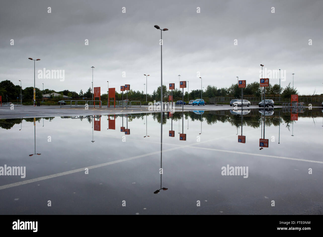 Un parcheggio allagato da heavy rain riflette il cielo e le vetture in un'immagine speculare in questo riassunto del paesaggio urbano. Foto Stock