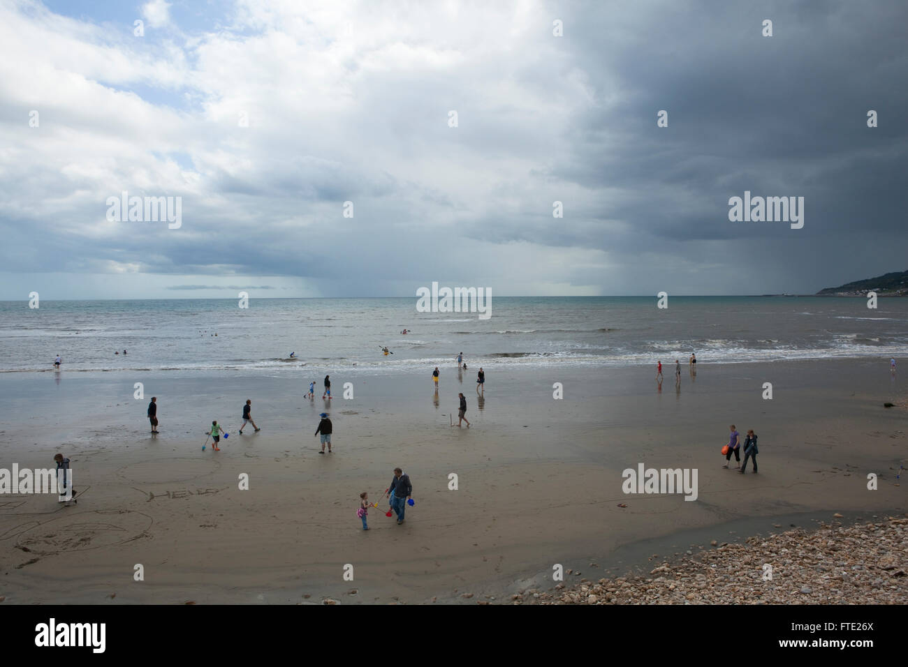 Vacanze a piedi e giocando sulla sabbia di una spiaggia britannico in una scena di tipico british estate meteo, umido e nuvoloso con una mancanza di sole. Foto Stock