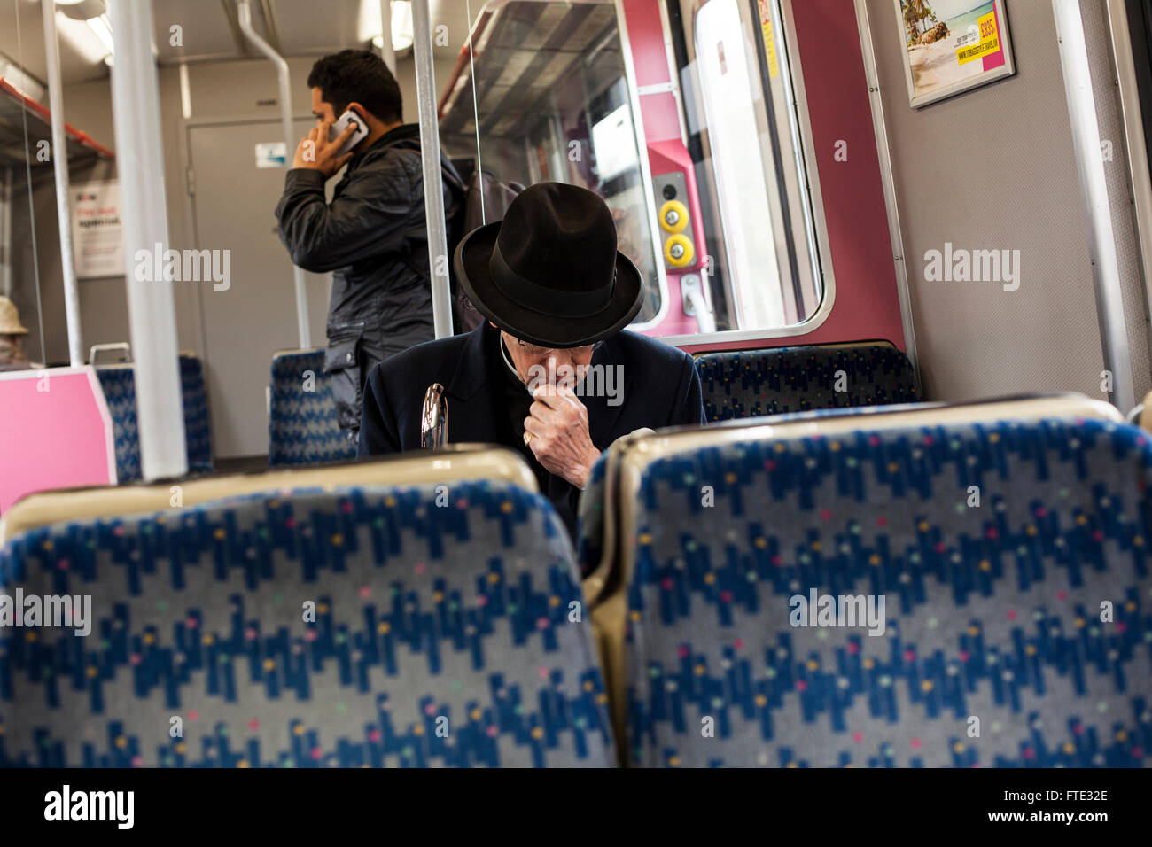 Un uomo con un cappello nero e il bastone da passeggio in treno in atto di pensare e di un altro uomo sullo sfondo di parlare per telefono Foto Stock