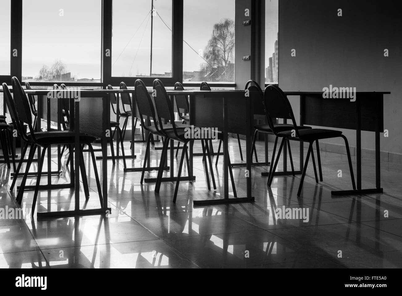 Righe e righe di conferenza vuota sedie catturati nella luce naturale del sole in una classe in ambiente scolastico. Immagine in bianco e nero wi Foto Stock