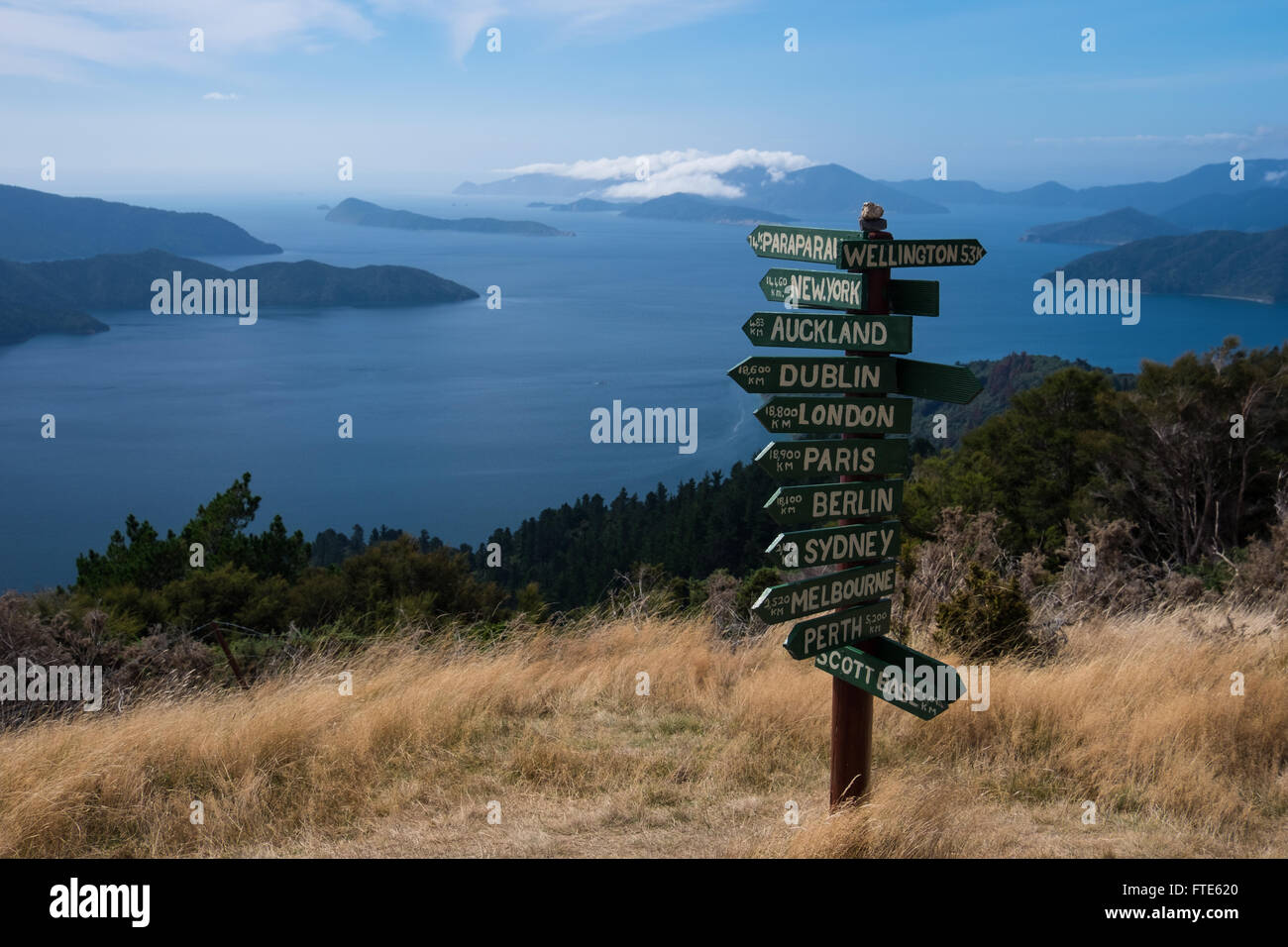 Un segno di post che mostra le distanze a vari luoghi con il Marlborough Sounds in background Foto Stock
