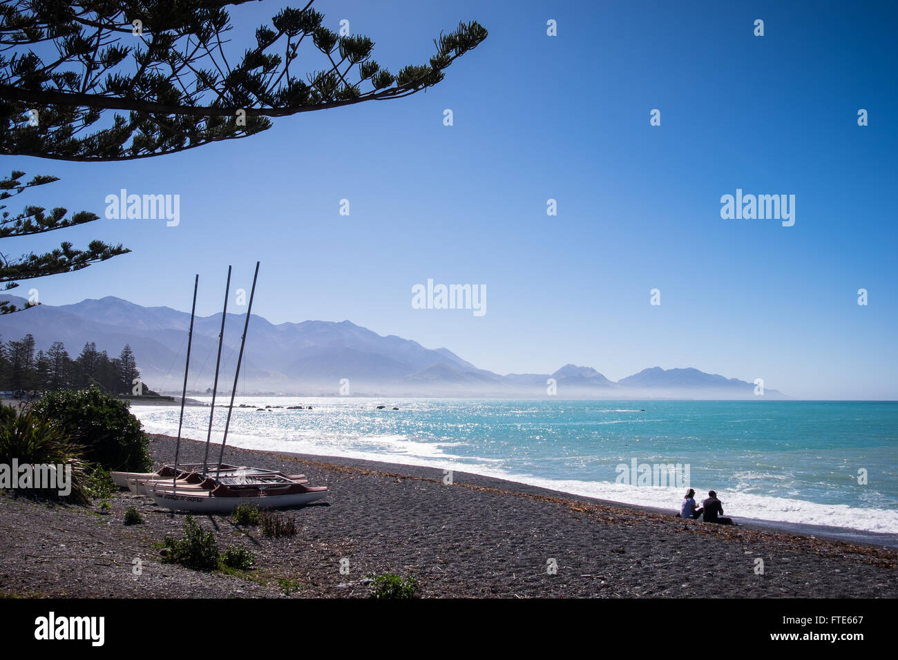 La gente seduta sulla spiaggia di Kaikoura guardando verso il Kaikoura Seaward Mountain Range Foto Stock