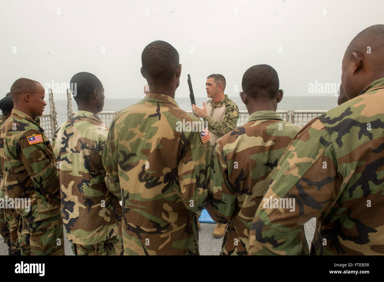 140305-N-ZY039-350 Monrovia, Liberia (7 marzo 2014) - Chief Master-at-Arms Bryan Roelike, un membro della sicurezza imbarcato a bordo del team joint ad alta velocità a nave USNS Spearhead (JHSV 1), spiega equipaggio servito armi ai membri della Liberia Guardia Costiera durante un giunto di familiarizzazione di esercitare sulla nave. Punta di diamante. Punta di diamante, U.S. Navy's first-in-class, comune ad alta velocità a vaso, è sulla sua fanciulla distribuzione teatro di supporto di sicurezza gli sforzi di cooperazione e collaborazione internazionali di programma per il potenziamento delle capacità, Africa Partnership Stazione, NEGLI STATI UNITI Sesta flotta area di operazioni. (Brevetto statunitense n. Foto Stock