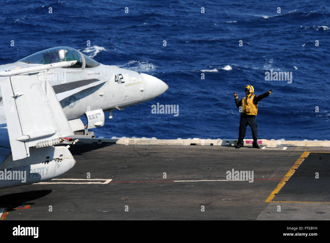 140315-N-CZ979-001 Mare Mediterraneo (15 marzo 2014) un marinaio dirige un'F/A-18C Hornet attaccato al "Golden guerrieri" di Strike Fighter Squadron (VFA) 87 come i taxi sul ponte di volo della portaerei USS George H.W. Bussola (CVN 77). George H. W. Bush è su una distribuzione programmata sostenere le operazioni di sicurezza marittima e di teatro la cooperazione in materia di sicurezza gli sforzi negli Stati Uniti Sesta flotta area di operazioni. (U.S. Foto di Marina di Massa lo specialista di comunicazione di terza classe Giosuè Card/rilasciato) Foto Stock