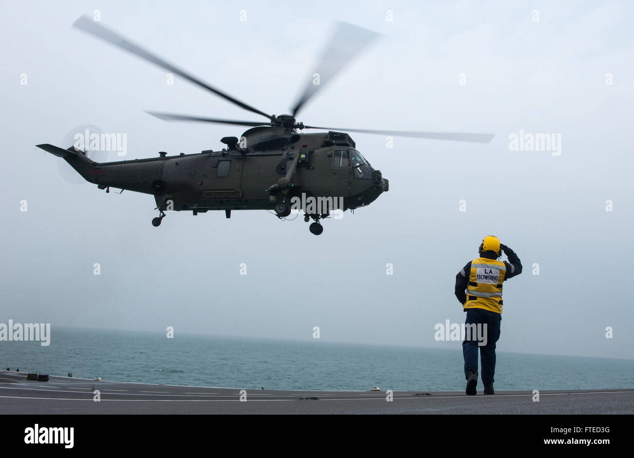 Un marinaio della Royal Navy saluta un Seaking Helicopter del 843 Naval Air Squadron durante l'esercitazione Joint Warrior 14-1 nel Mare del Nord. Questo esercizio annuale di addestramento militare migliora l'interoperabilità della NATO ed è progettato per preparare le forze alleate alle operazioni globali. Foto Stock