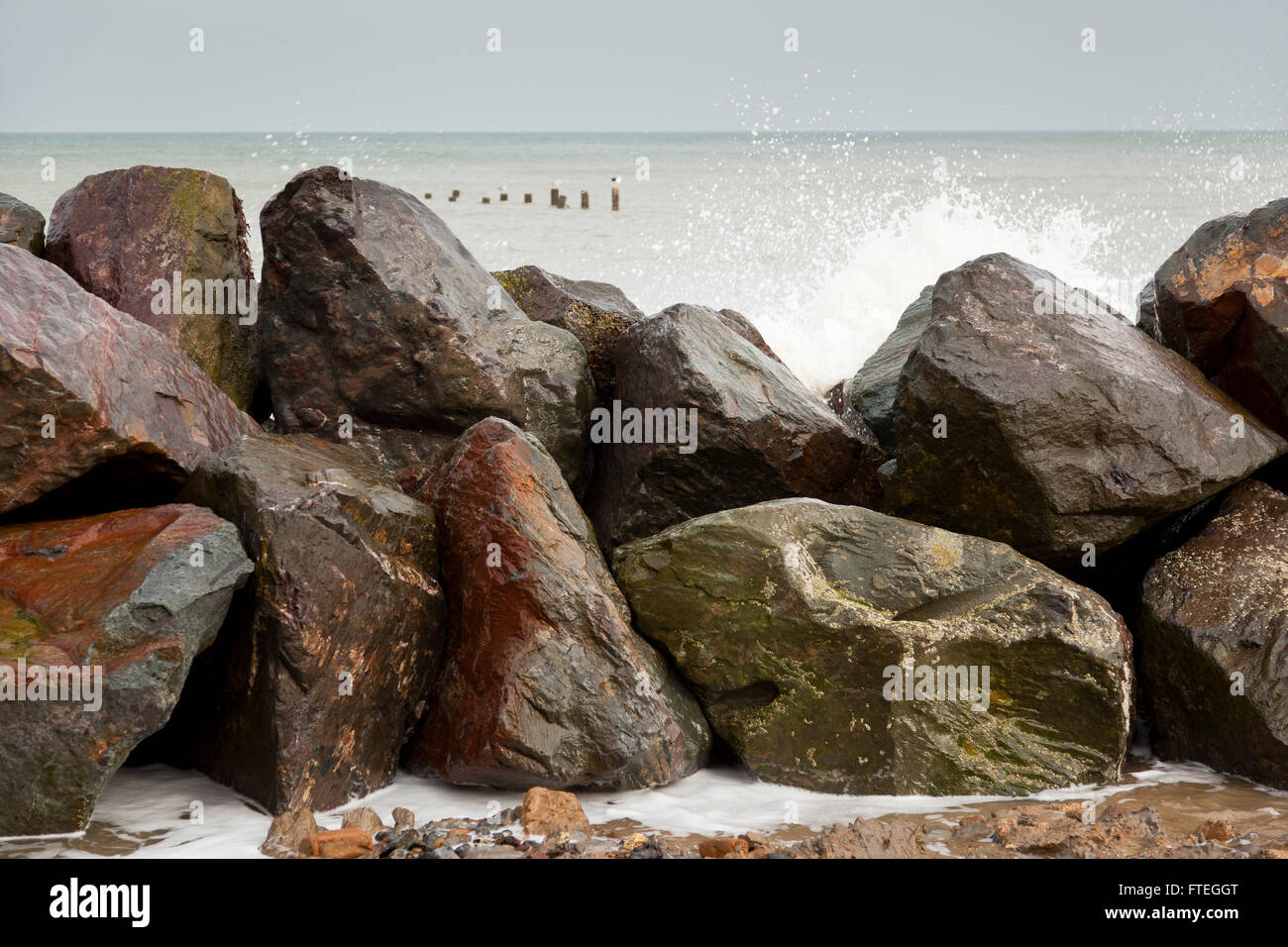 Onde che spruzzano contro le difese rocciose del mare a Happisburgh, Norfolk, Regno Unito Foto Stock