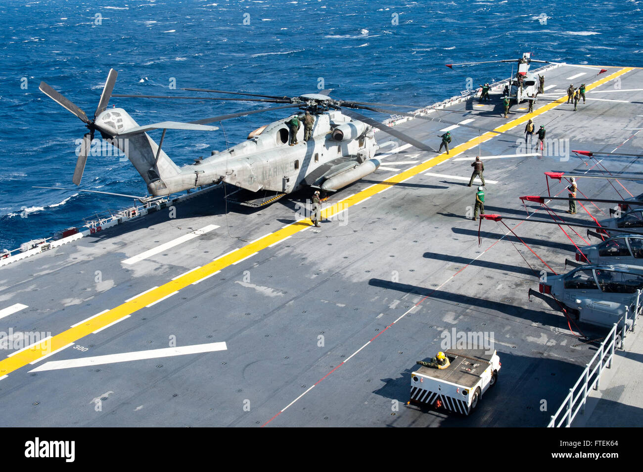 Marinai e Marines a bordo della USS Iwo Jima preparano un elicottero CH-53E Super Stallion e un elicottero AH-1W Super Cobra per lo stivaggio durante le operazioni nel Mar Mediterraneo, sottolineando la coordinazione tra il personale della Navy e del Marine Corps. Foto Stock