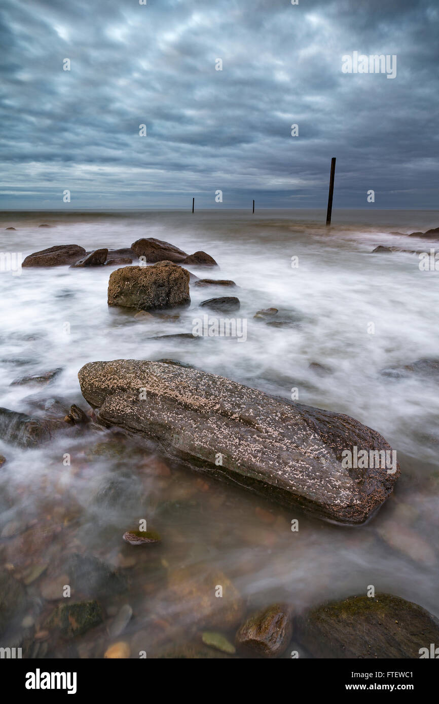 Lynmouth Beach, Devon, Inghilterra, è coperto di rocce e ciottoli. Quando il mare arriva in onde swirl intorno alle rocce. Foto Stock