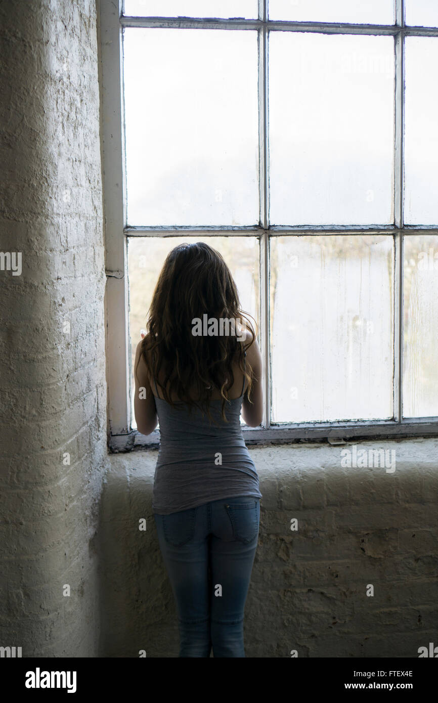 Vista posteriore di una giovane donna che guarda fuori dalla finestra Foto Stock