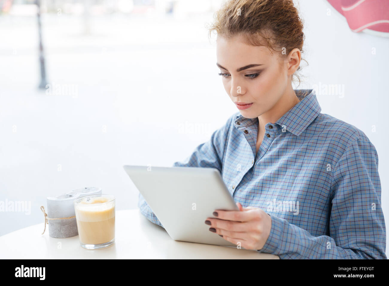 Concentrato bella giovane donna a bere caffè e utilizzo di tablet in cafe Foto Stock