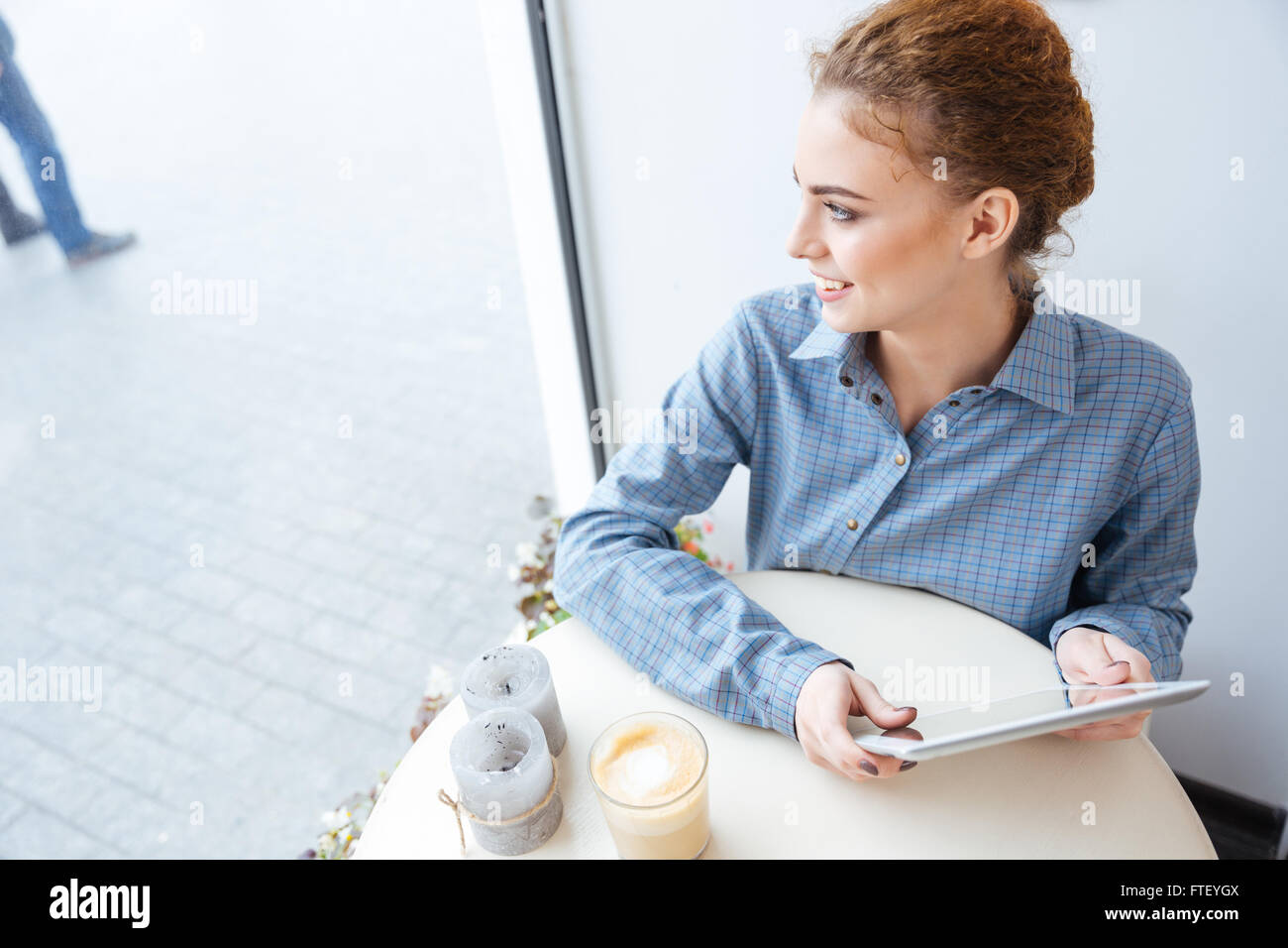 Allegro affascinante giovane donna utilizzando tablet e guardando la finestra in cafe Foto Stock