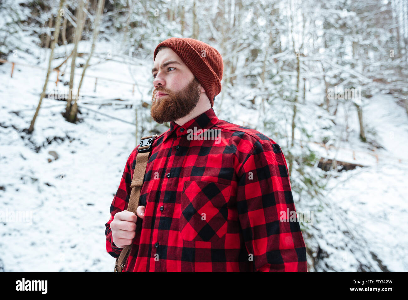 Ritratto di grave barbuto Giovane Uomo in camicia chekecred e hat con zaino  in montagna in inverno forest Foto stock - Alamy