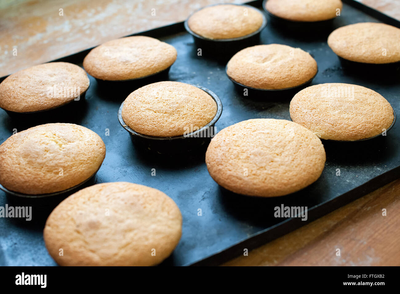 Close up ancora la vita di decine di freschi di forno muffin semplice raffreddamento in singole lattine sulla teglia sul tavolo di legno Foto Stock