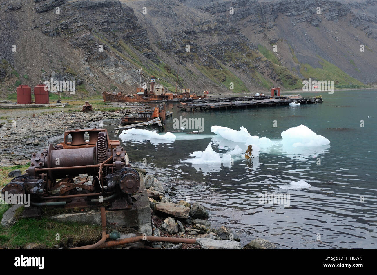 Una caccia alla balena spiaggiata barca, altri macchinari, dei serbatoi di stoccaggio e il ghiaccio sulla spiaggia nelle rovine di Grytviken stazione baleniera. Foto Stock