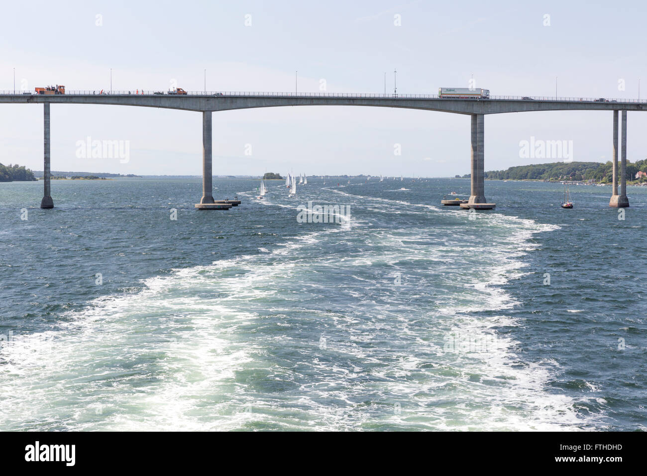 Il ponte Svendborgsund e barche a vela seguendo la scia di un traghetto passeggeri nel porto di Svendborg, Danimarca Foto Stock