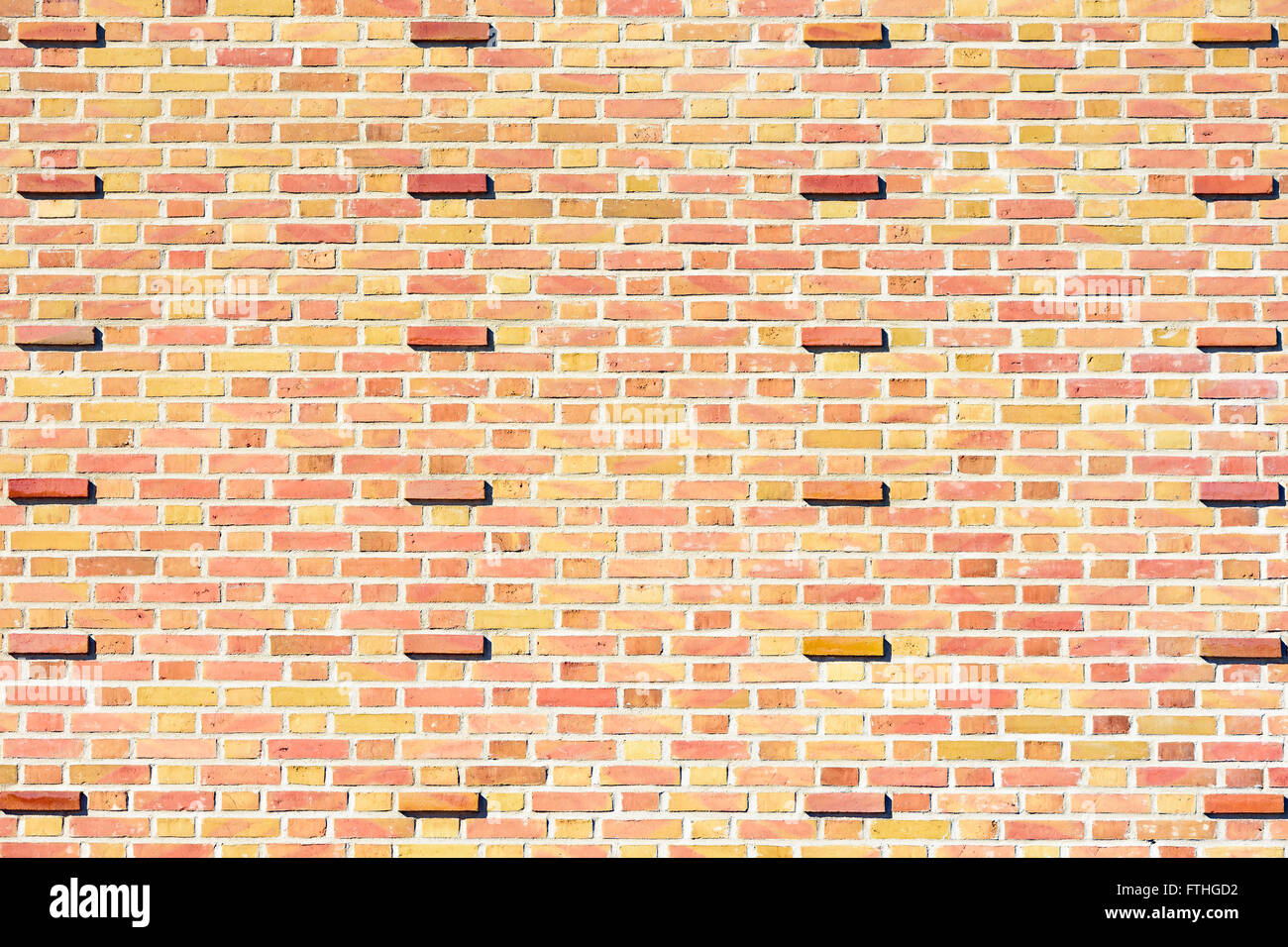 Giallo pallido e rosso mattone con il muro di mattoni sporgenti ad intervalli. Sfondo interessante. Foto Stock