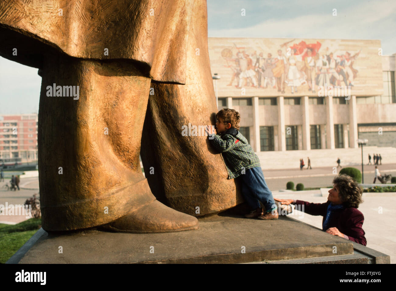 Ragazzo giovane incoraggiato da sua madre, baciare i piedi della statua di Enver Hoxha, il fondatore di stato comunista, Tirana, 1990 Foto Stock