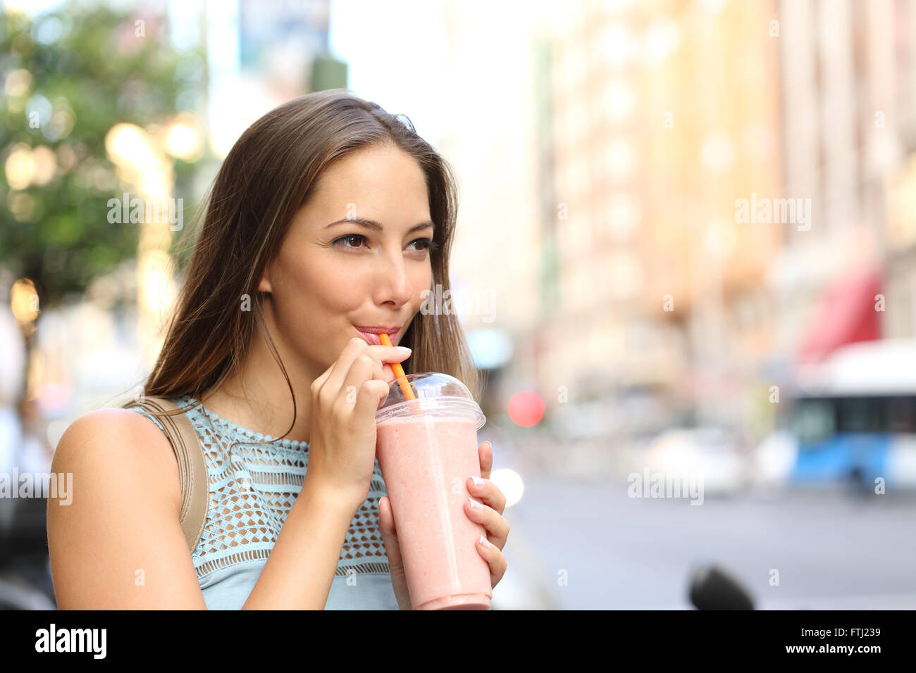 Malinconici donna felice sorseggiando un frullato in strada Foto Stock