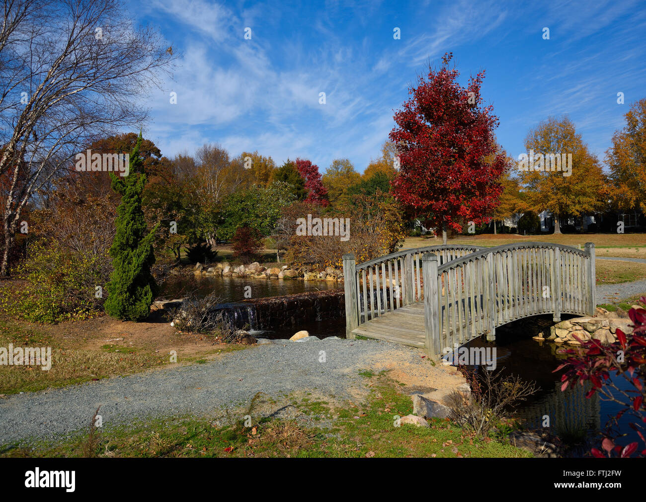 Il vecchio ponte pedonale che attraversa un piccolo ruscello in un parco con i colori autunnali. Foto Stock