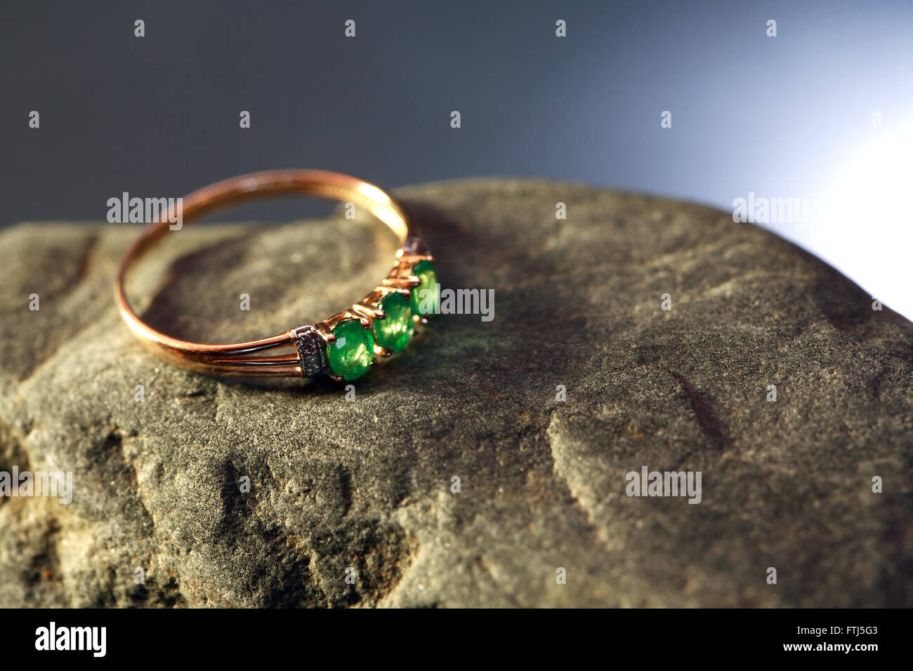 Anello in oro con smeraldo sulla pietra grigia contro bello sfondo scuro Foto Stock