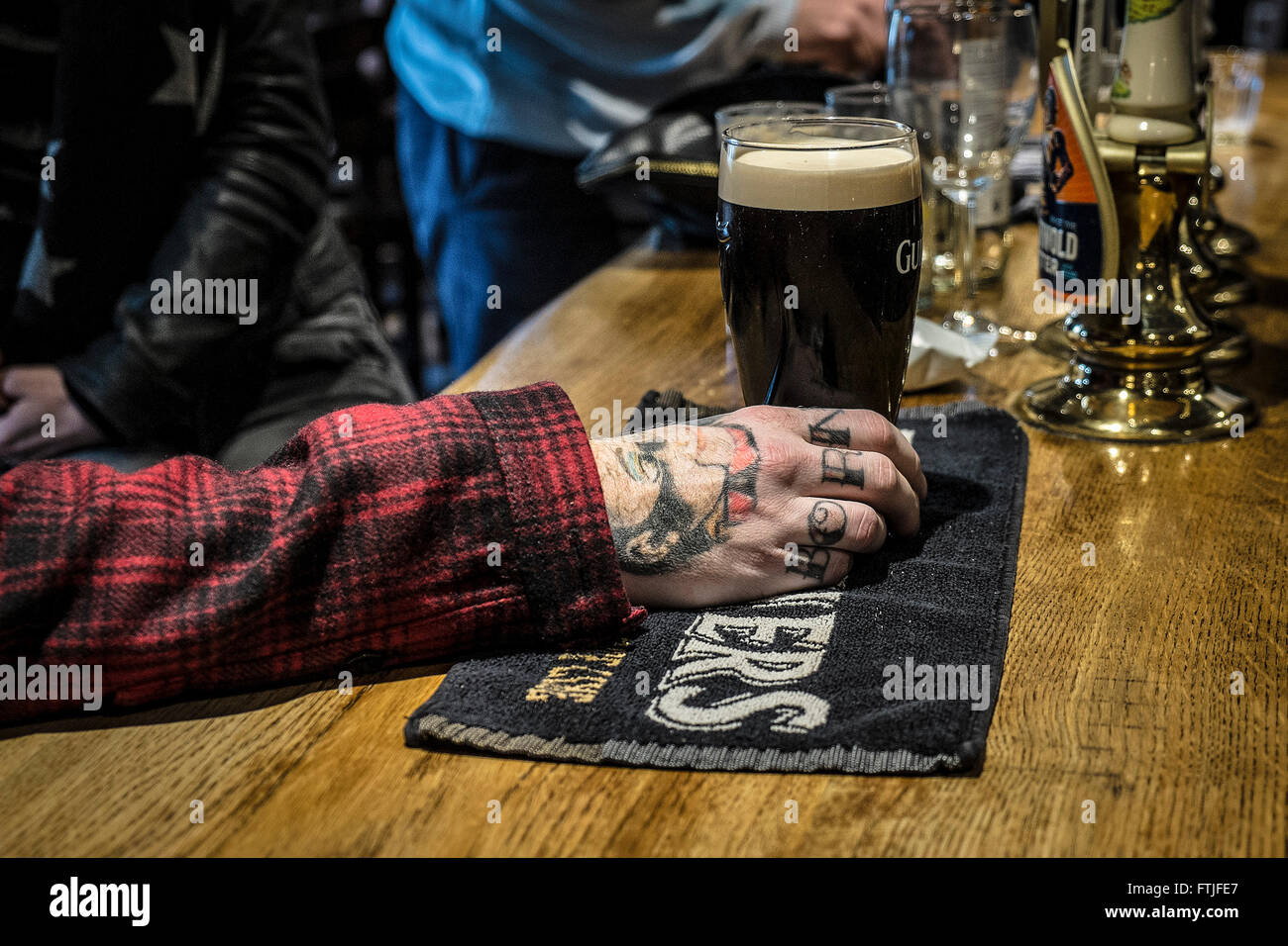 Un cliente è tatuato mano che tiene una pinta di Guinness in un tradizionale pub inglese in Essex. Foto Stock