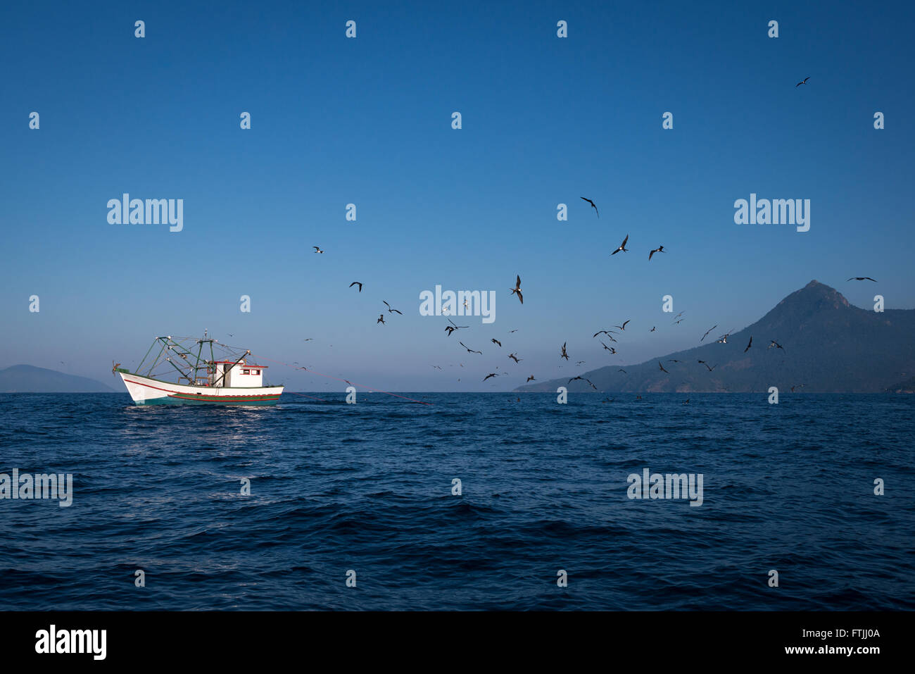 Una barca da pesca trascinando un gambero net off Ilhabela, se il Brasile. Uccelli come sule e frigatebirds sono i seguenti per ottenere il rottame Foto Stock
