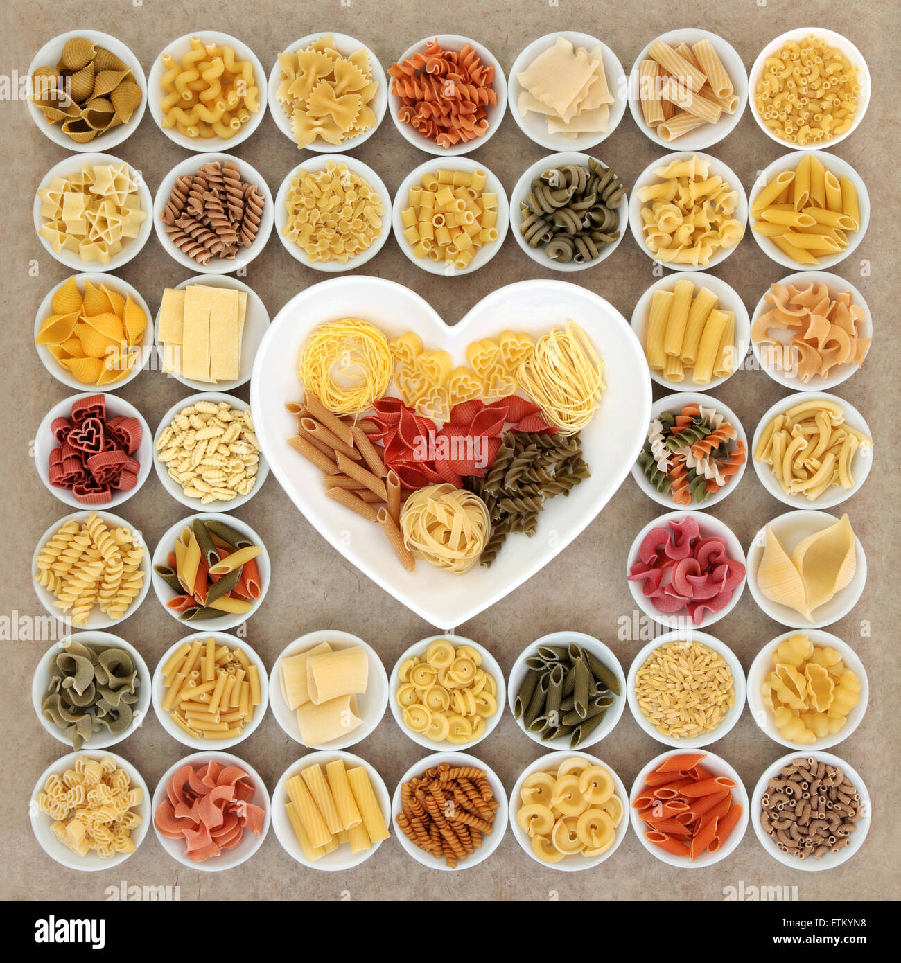 La pasta secca spaghetti varietà alimentare nel round ciotole di porcellana a forma di cuore piatto sulla canapa naturale sfondo della carta. Foto Stock