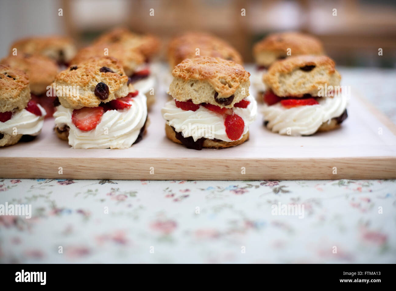 Focaccine di frutta con panna e lampone ripieno su una tavola di legno su una tovaglia floreale in una panetteria Foto Stock