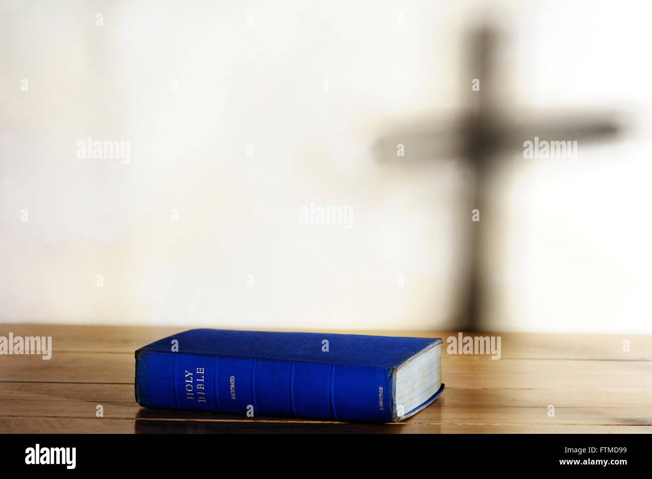 Vecchia copia della Sacra Bibbia giacente su una tabella con l'ombra di una croce sul background. Foto Stock