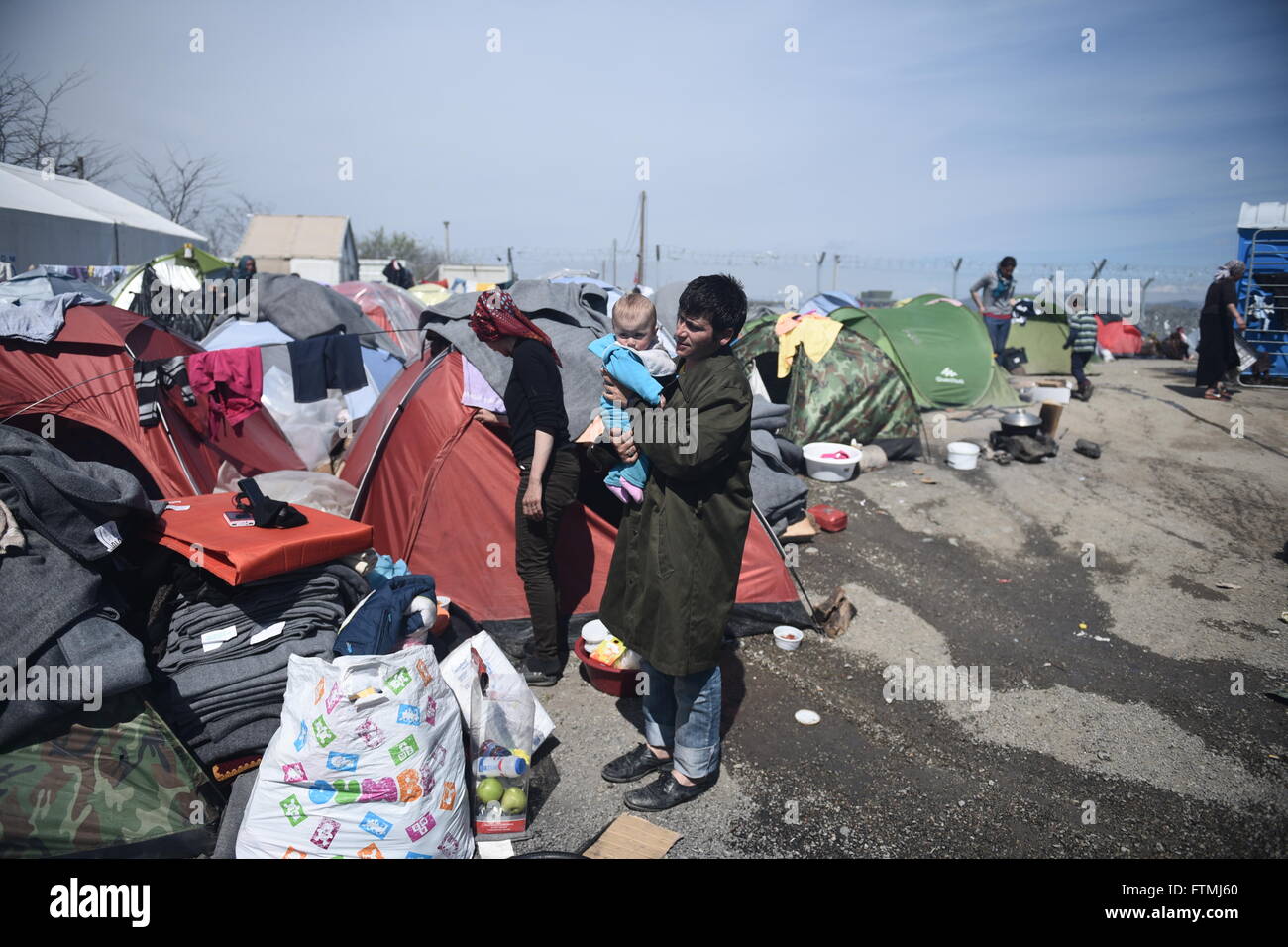 Un uomo che sostiene il suo bambino, come rifugiati e migranti rimangono bloccati al chiuso greco confine macedone, vicino del nord del villaggio greco di Idomeni. Foto Stock