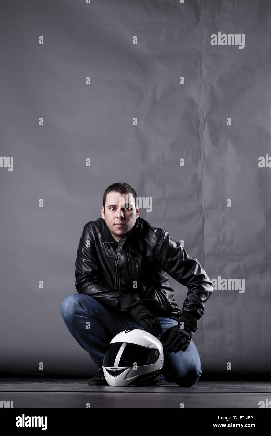 Automobilista con un casco, giacca di pelle e jeans, su sfondo grunge con illuminazione difficili Foto Stock Automobilista con un casco, giacca di pelle e jeans, su sfondo grunge con illuminazione difficili Foto Stock