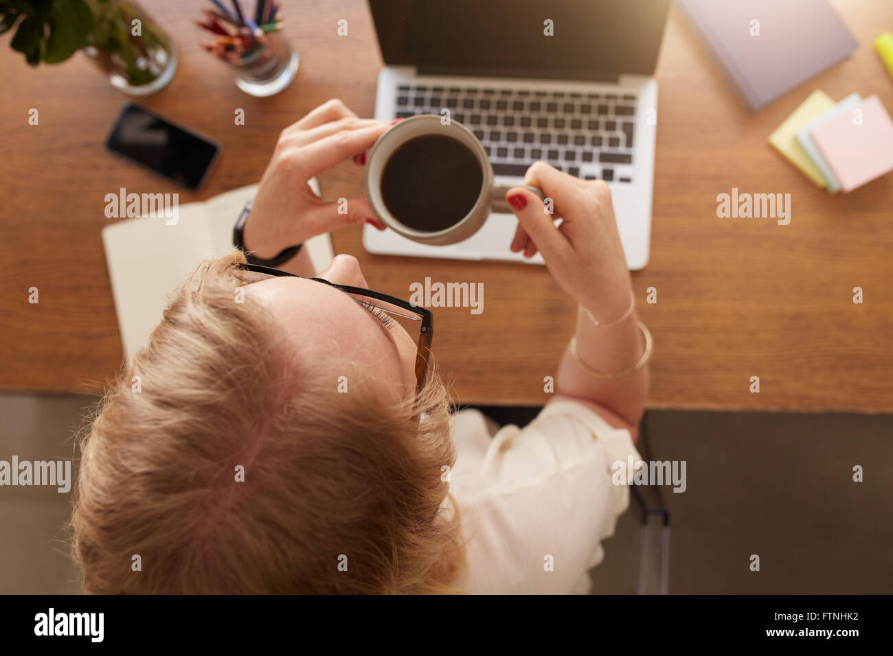 Vista aerea della donna di bere il caffè mentre è seduto alla sua scrivania in ufficio a casa. Foto Stock