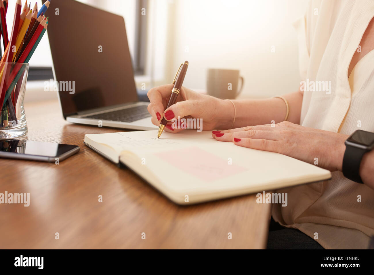 Chiudere l immagine della donna seduta alla sua scrivania e scrivere le note. Imprenditrice lavora da casa in ufficio. Foto Stock