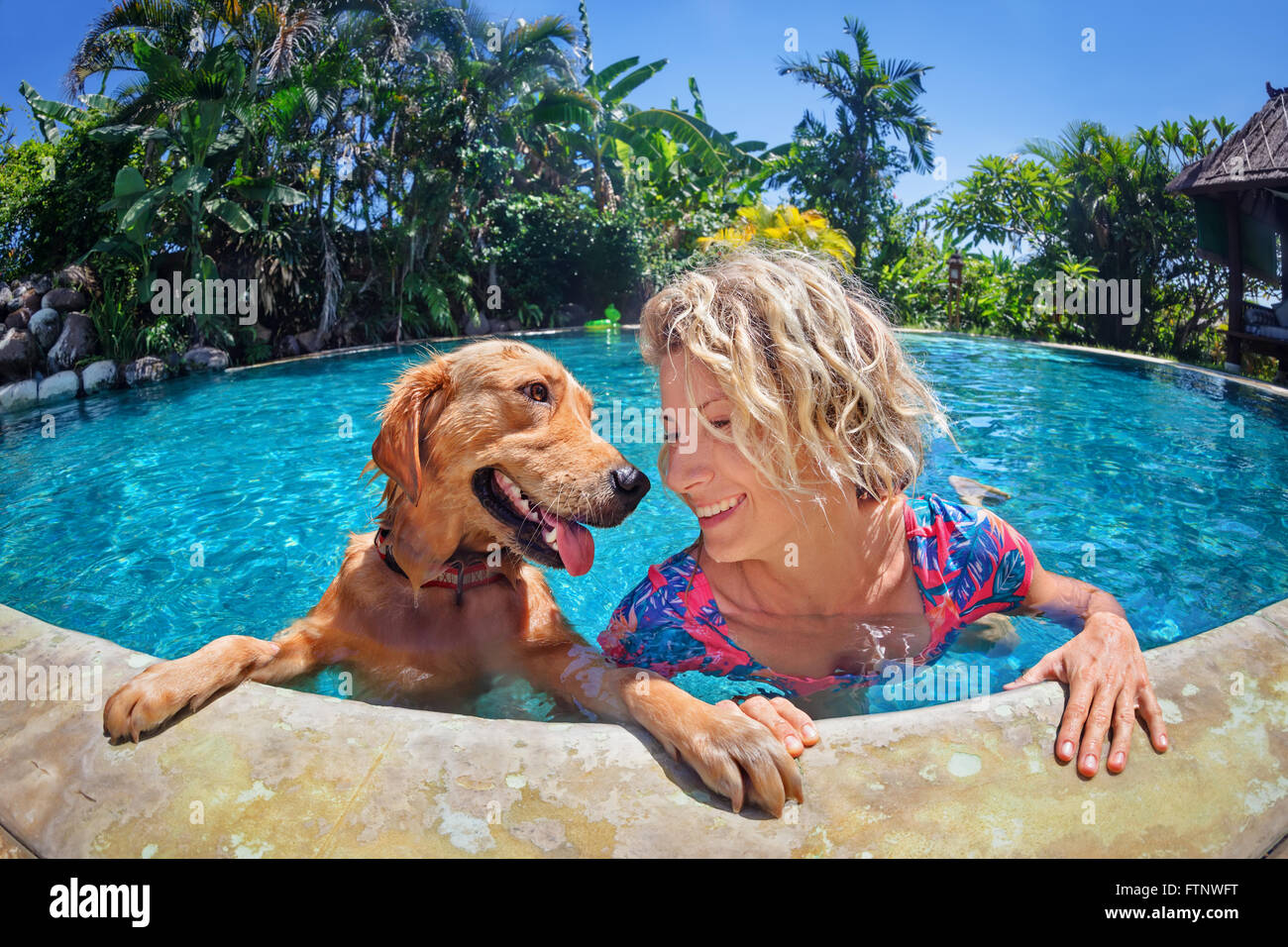 Divertente ritratto di donna smiley giocando con il divertimento e la formazione cucciolo di golden retriever della piscina esterna. Foto Stock