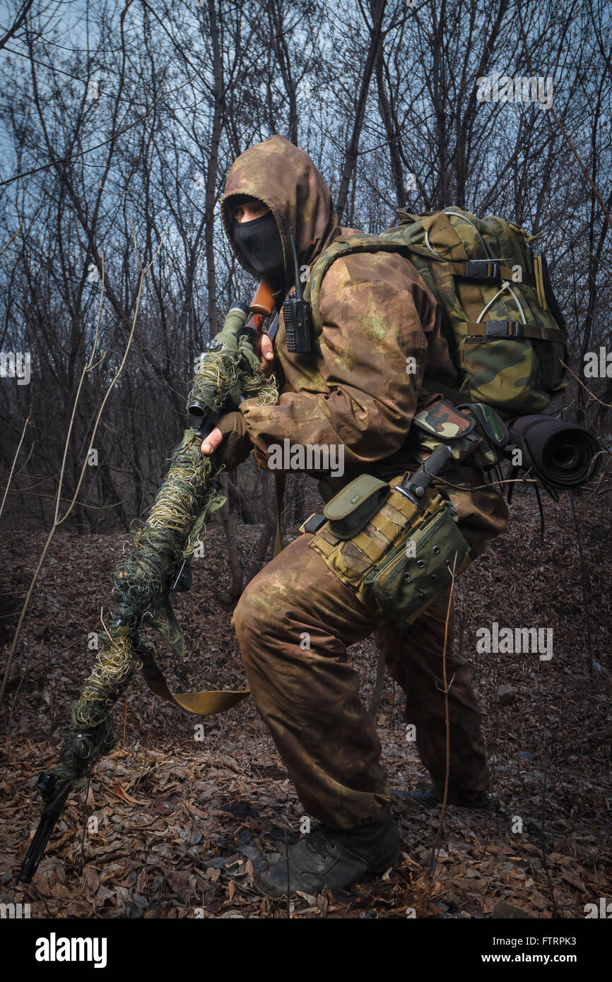 Sniper indossare tuta mimetica con un fucile a piedi nei boschi Foto Stock