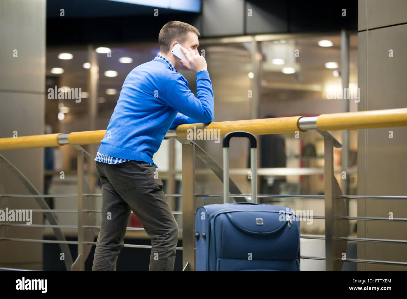 Giovane bello ragazzo indossa uno stile informale vestiti a piedi nella moderna stazione airport. Traveler di effettuazione della chiamata utilizza lo smartphone Foto Stock