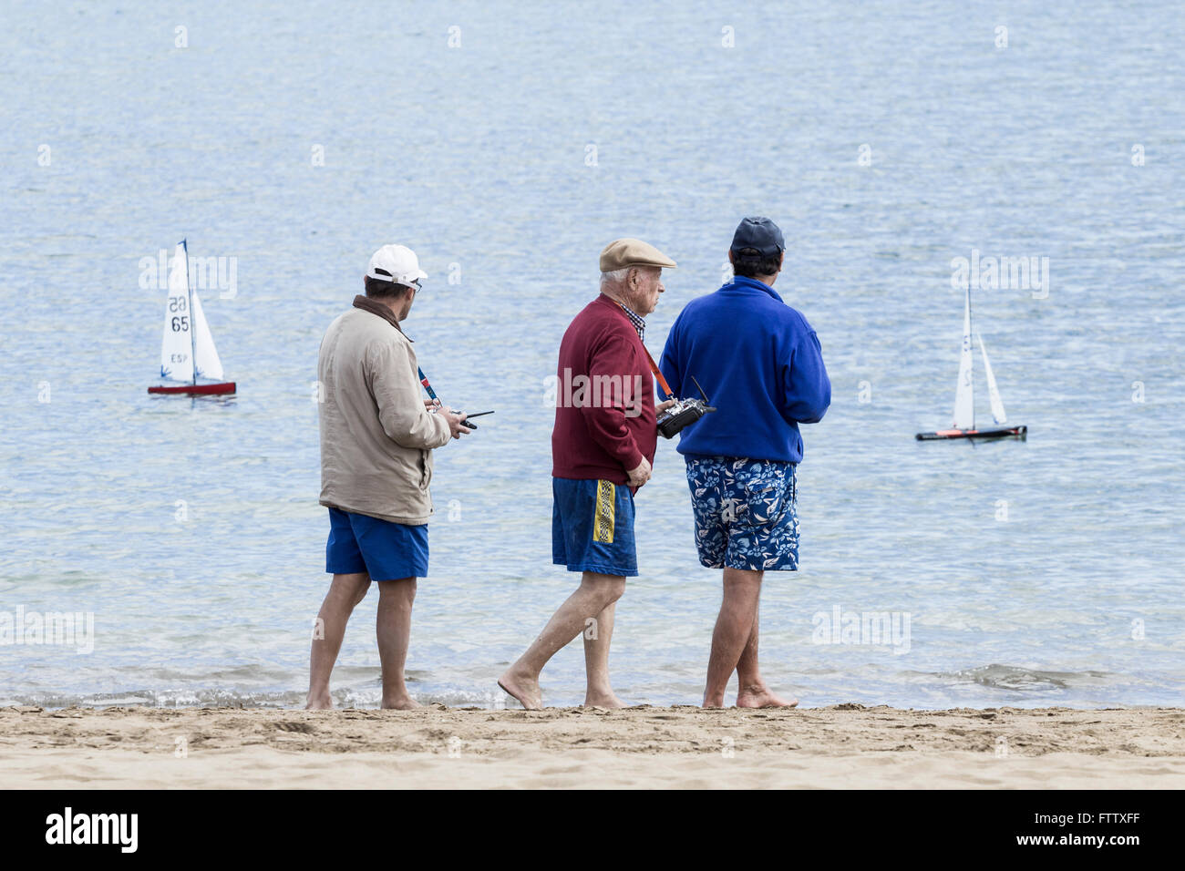 Uomini anziani in Spagna a piedi lungo la spiaggia racing radio controlled yachts. Foto Stock