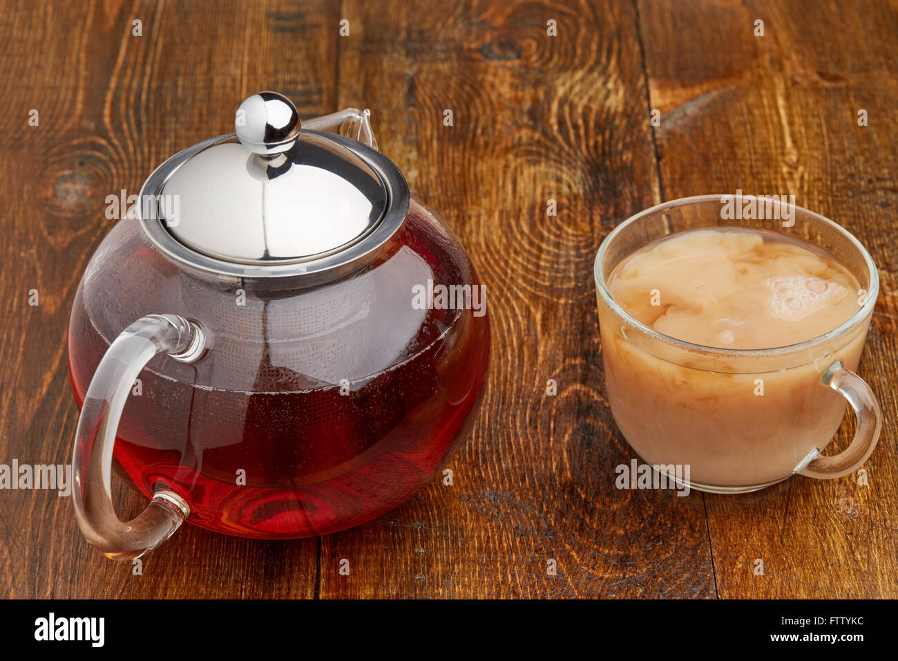 Set di vetro teiera e tazzina di tè nero con il latte sul tavolo di legno Foto Stock