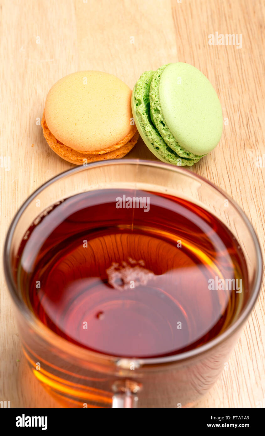 Impostare amaretti colorato e vetro tazza di tè nero su sfondo di legno Foto Stock