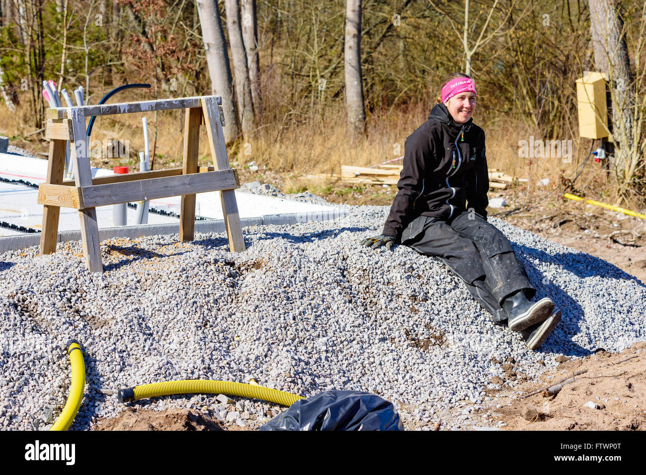 Ronneby, Svezia - Marzo 26, 2016: Femmina lavoratore edile di sedersi su un mucchio di ghiaia al resto nel sole di primavera. Casa trovati Foto Stock