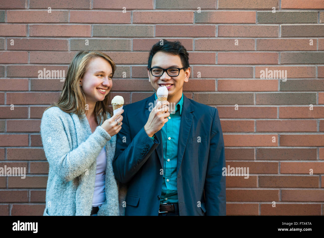 Due giovani sorridenti persone azienda coni gelato in piedi vicino a un muro di mattoni e in chat Foto Stock