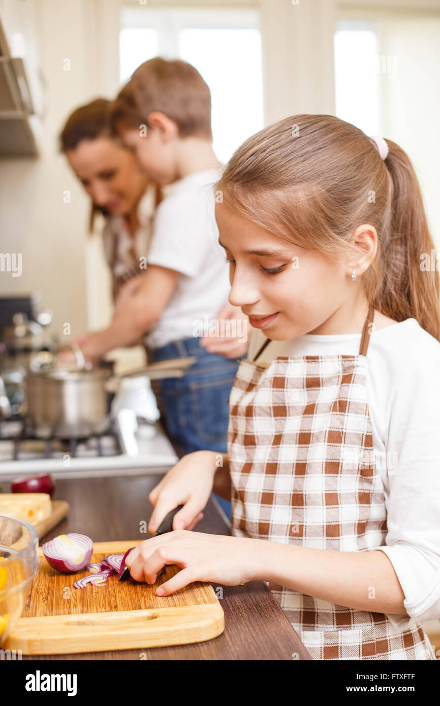 Cucina di famiglia dello sfondo. Giovani sorridente ragazza adolescente il taglio di cipolla. La mamma e i bambini in cucina Foto Stock