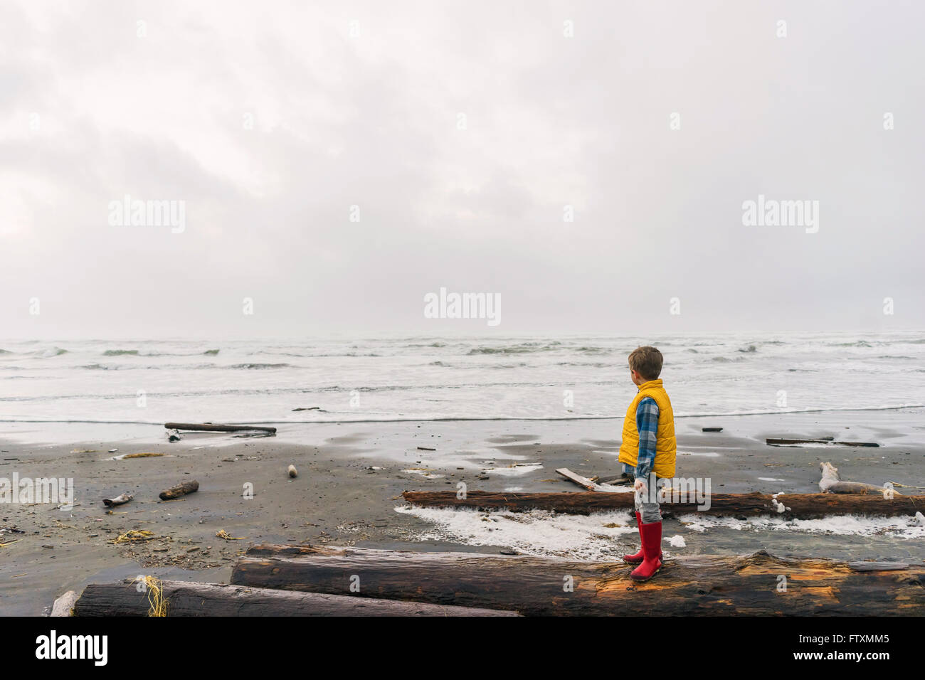 Ragazzo che sta su log che guarda al mare Foto Stock