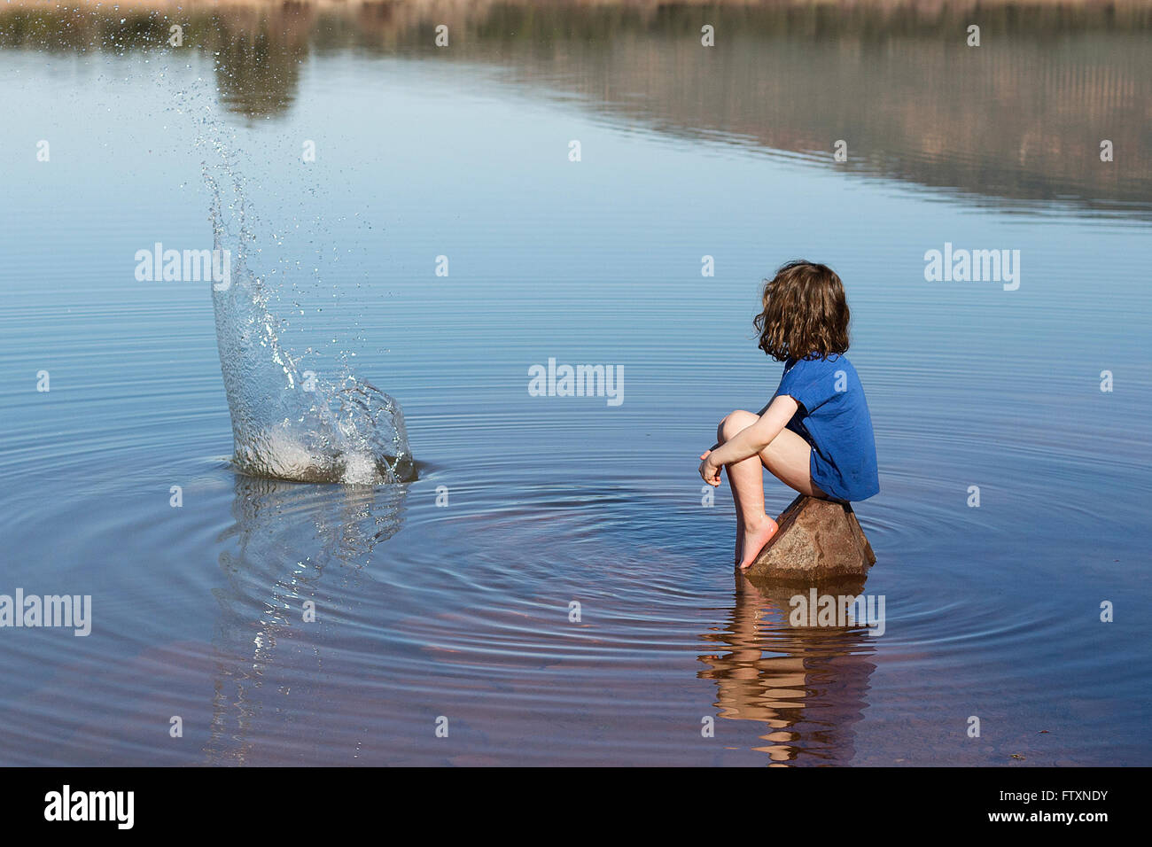 Ragazza seduta su di una roccia di gettare la pietra nel lago Foto Stock