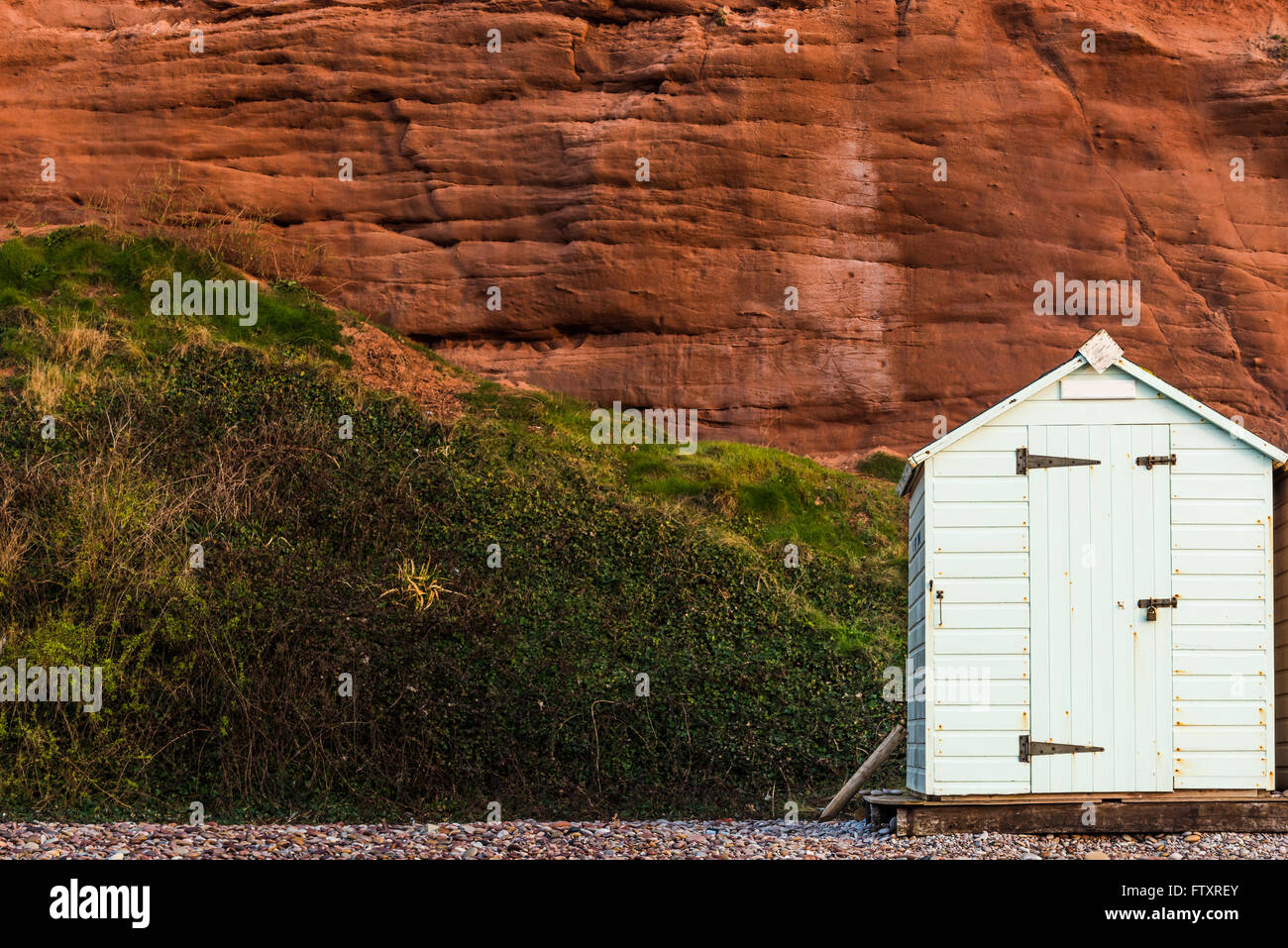 Beach Hut fila in colori pastello, roccia rossa sfondo, South Devon, Regno Unito Foto Stock