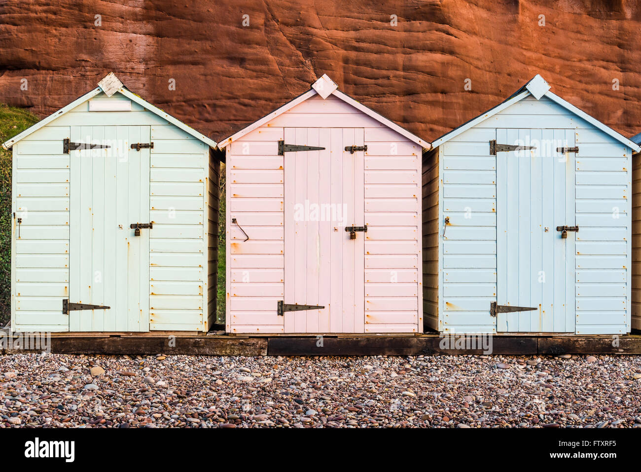 Beach Hut fila in colori pastello, roccia rossa sfondo, South Devon, Regno Unito Foto Stock